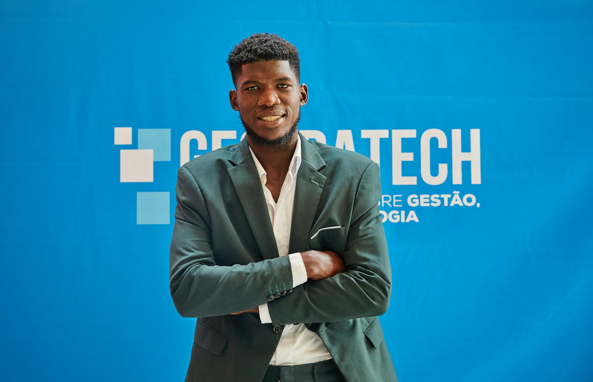 Businessman in suit smiling confidently with arms crossed at a technology event.